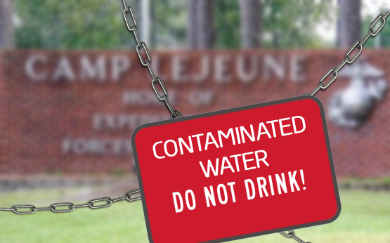 A warning street sign that says "Contaminated Water. Do Not Drink" held up by chains in front of the Camp Lejeune entrance sign.