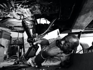 A mechanic examines a Mercedes vehicle from underneath, illuminating a possible defect.