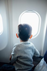 a child on an airplane seat looking out the window.