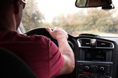 A man clutches his steering wheel as he drives down a road.