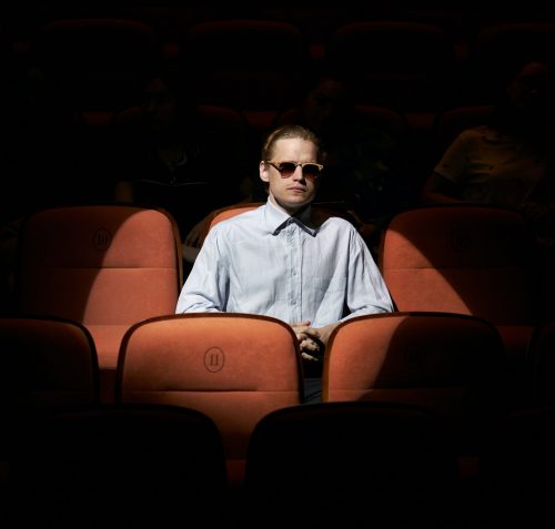 A spotlight illuminates a man sitting in the theater. There is no one sitting around him.