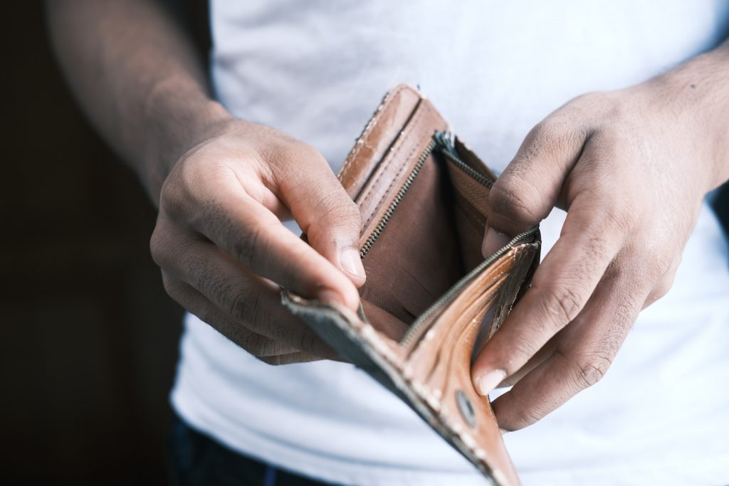 Man checks his wallet to find there is no money because, and is likely in debt.