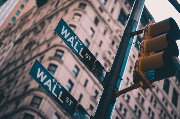 A street sign reading Wall Street with a large building behind it.