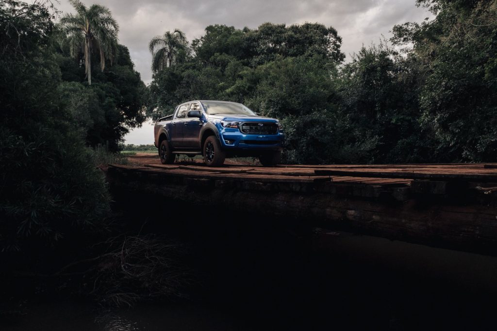 a blue Ford truck drives over a wooden bridge in the jungle.