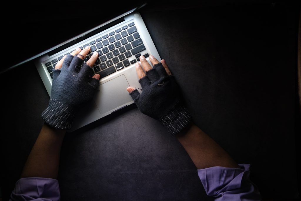 a person with fingerless gloves, presumably a robber, looms over a laptop.
