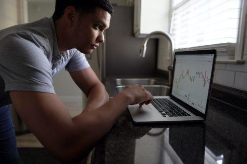 A man hunches over his laptop looking at investment figures on a market platform.