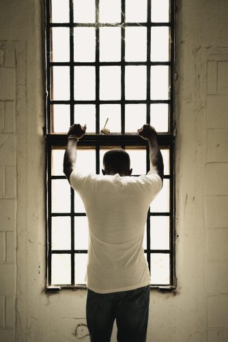 A black man bares his hands on a barred wall in a juvenile center.